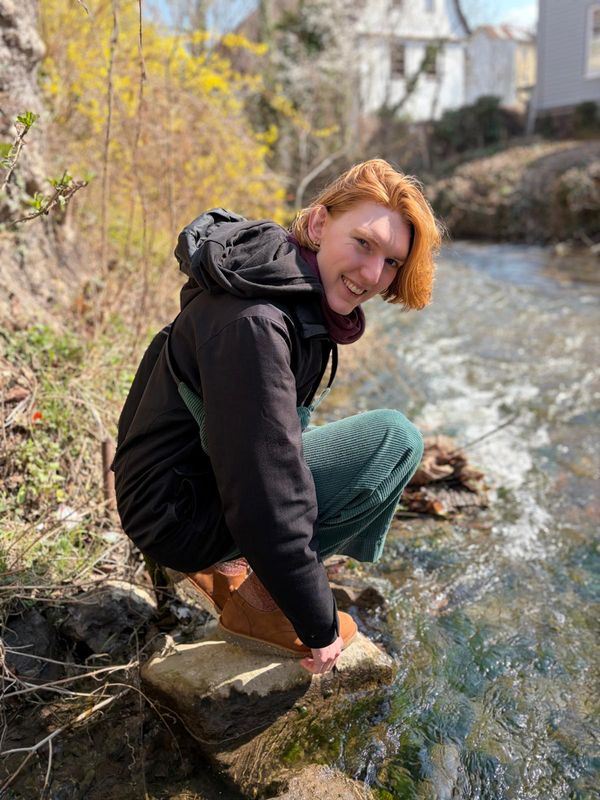 Hens hockt am Ufer eines Bachs und dreht sich lächelnd zur Kamera